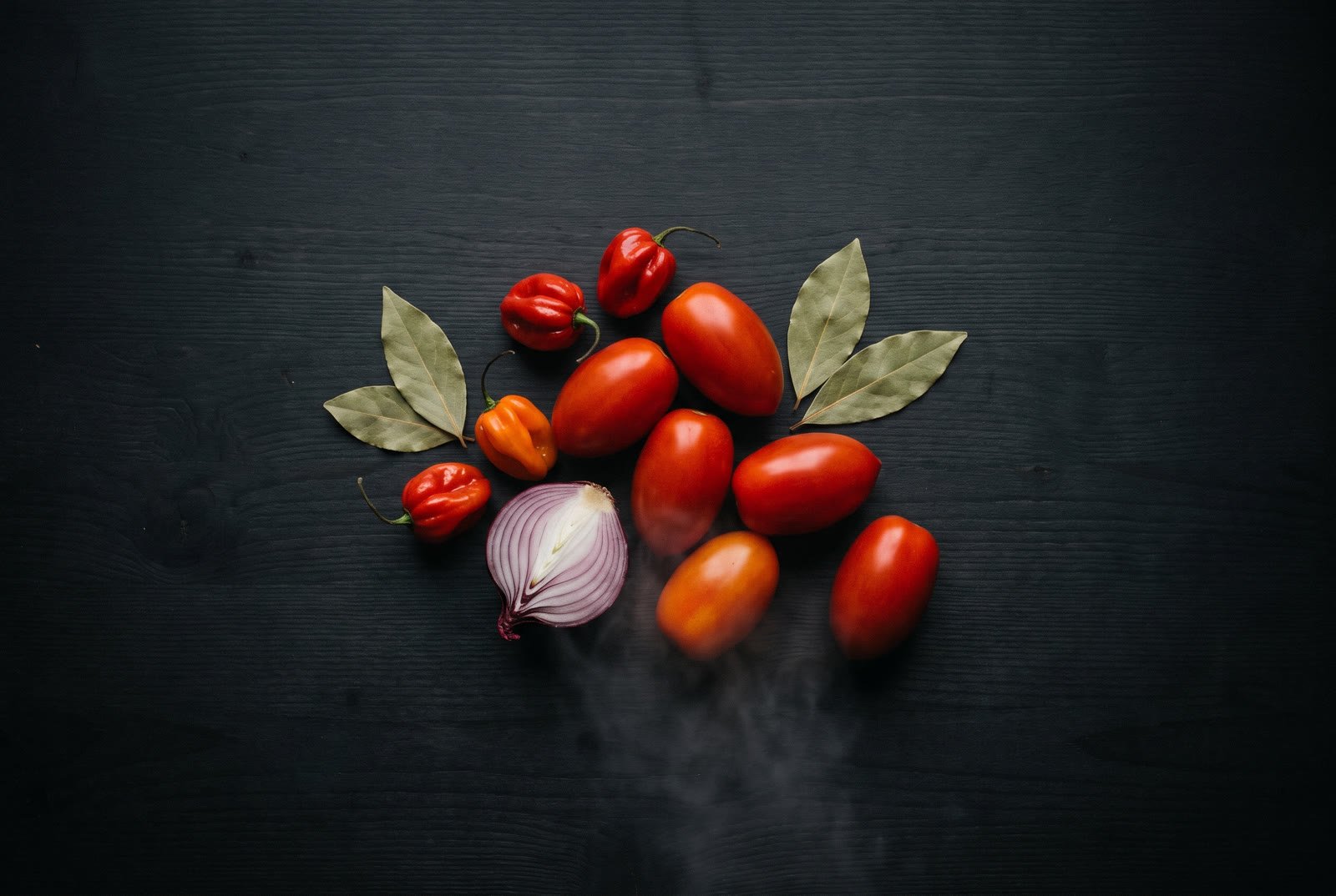 Plum tomatoes, scotch bonnet peppers and red onion on dark wood